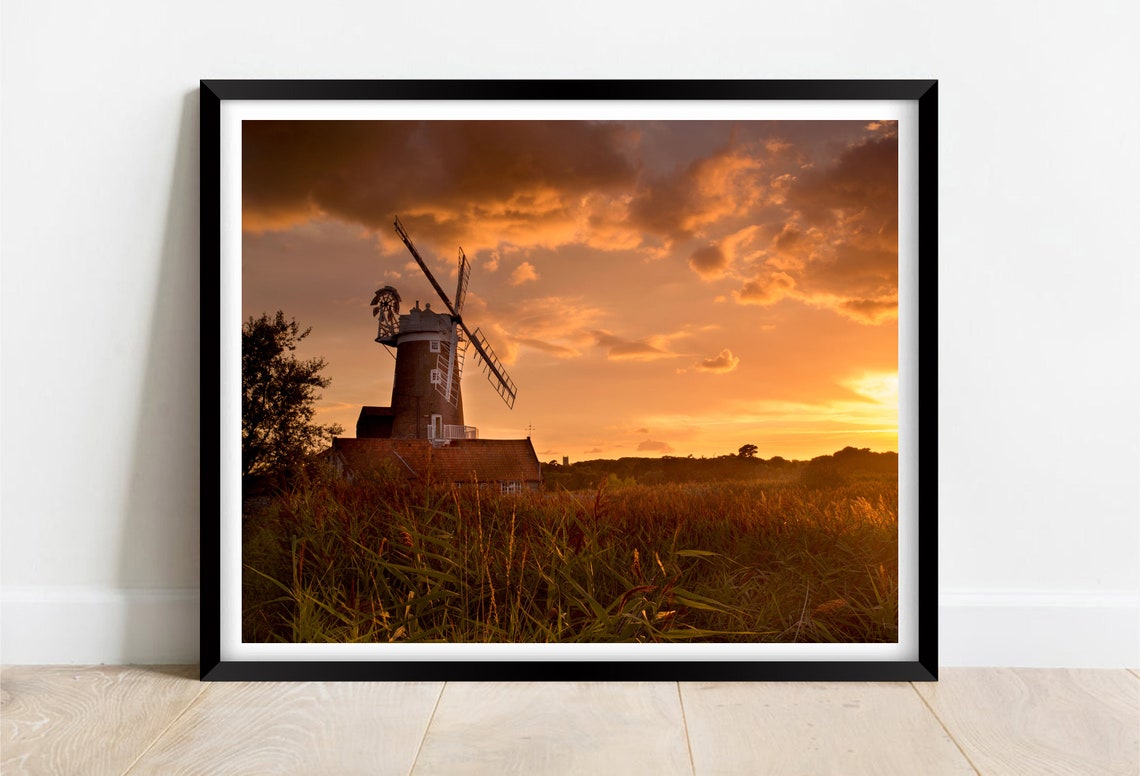 Historic Windmill Silhouetted Against a Fiery Orange Sunset Sky Poster