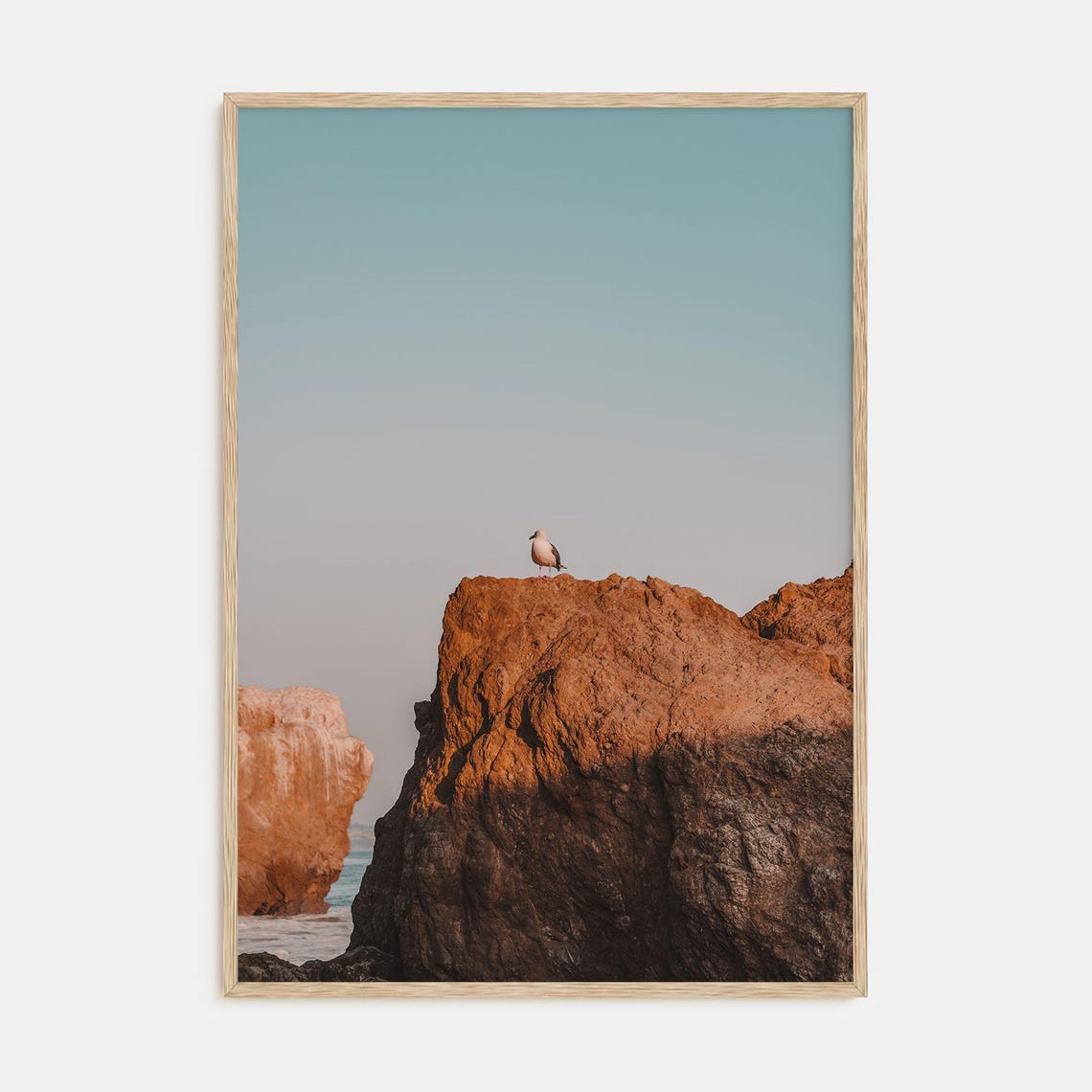 Lone Seagull Perched on a Red Rock Formation at the Beach Poster