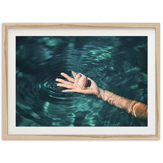 Hand Holding Seashell Over Teal Ocean Water Photography Poster