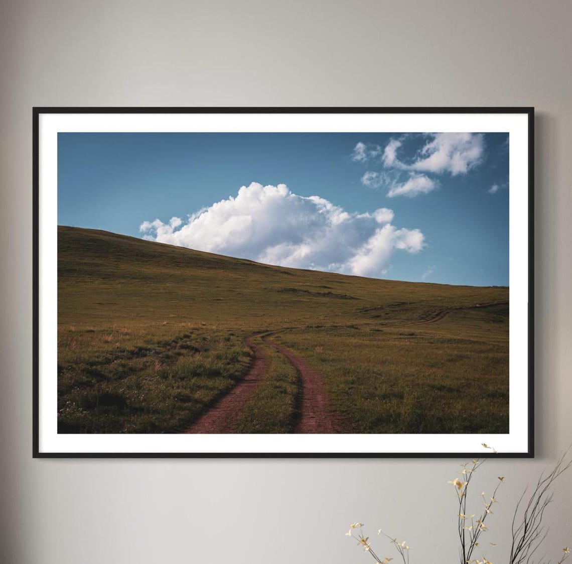 Winding Dirt Road Across Open Grassland Under Blue Sky Poster