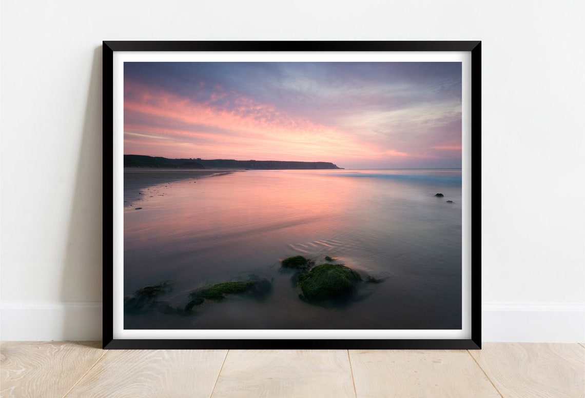 Soft Pink Sunset Over a Calm Shoreline with Mossy Rocks Poster