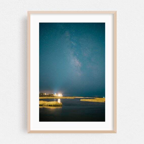 Starry Night Sky Over Still Coastal Waters With Distant Lights Art Print