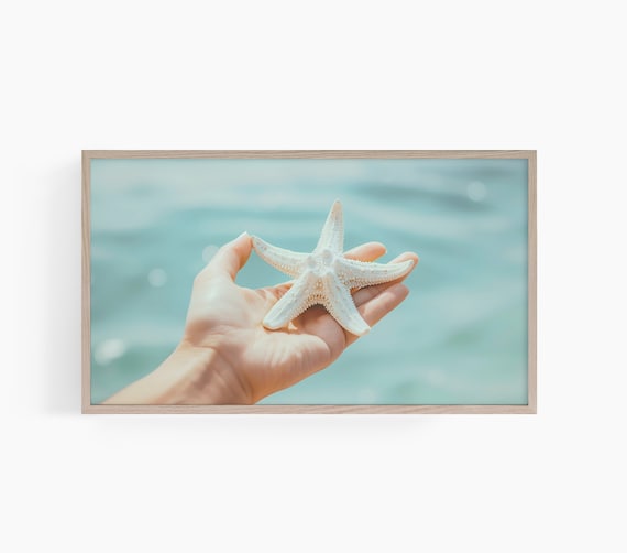 Hand Gently Holding a White Starfish Over the Turquoise Sea Poster