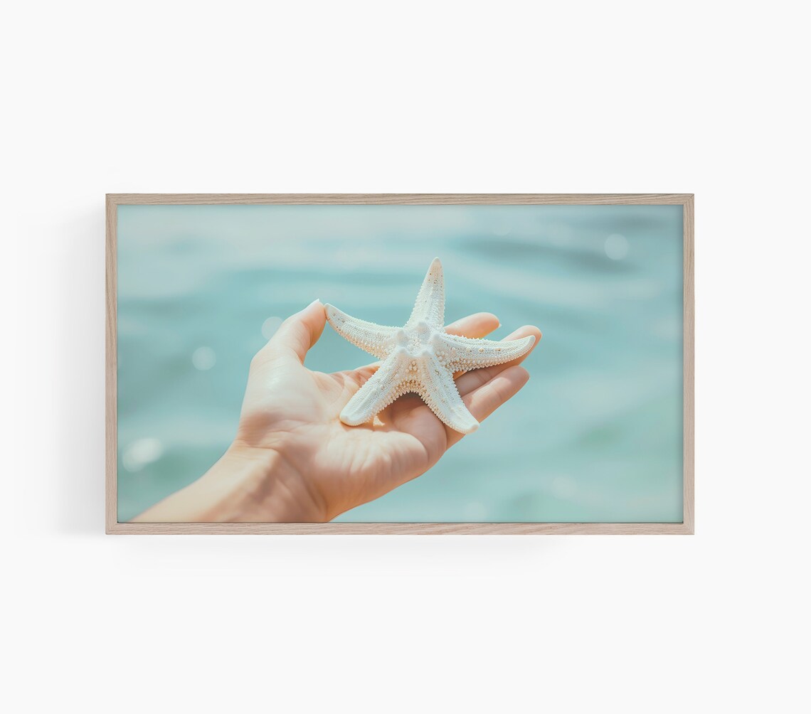 Hand Gently Holding a White Starfish Over the Turquoise Sea Poster