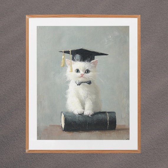 White Kitten in Graduation Cap with Bow Tie Sitting on Book Poster